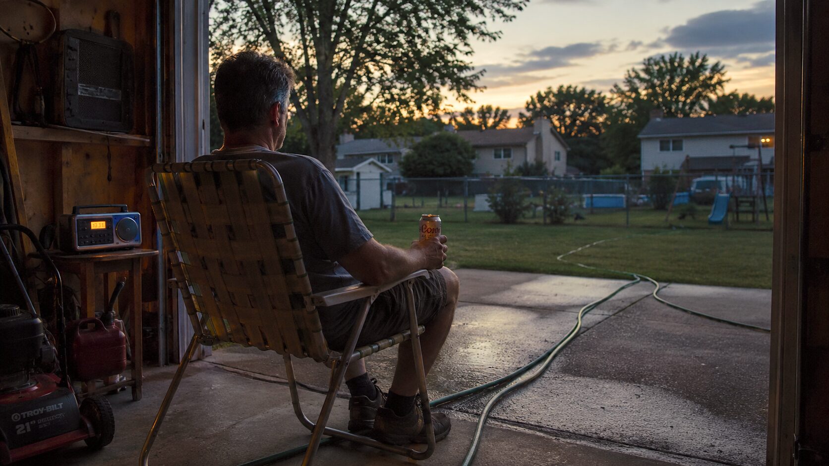A father sits in a garage at golden hour, looking out at the yard.